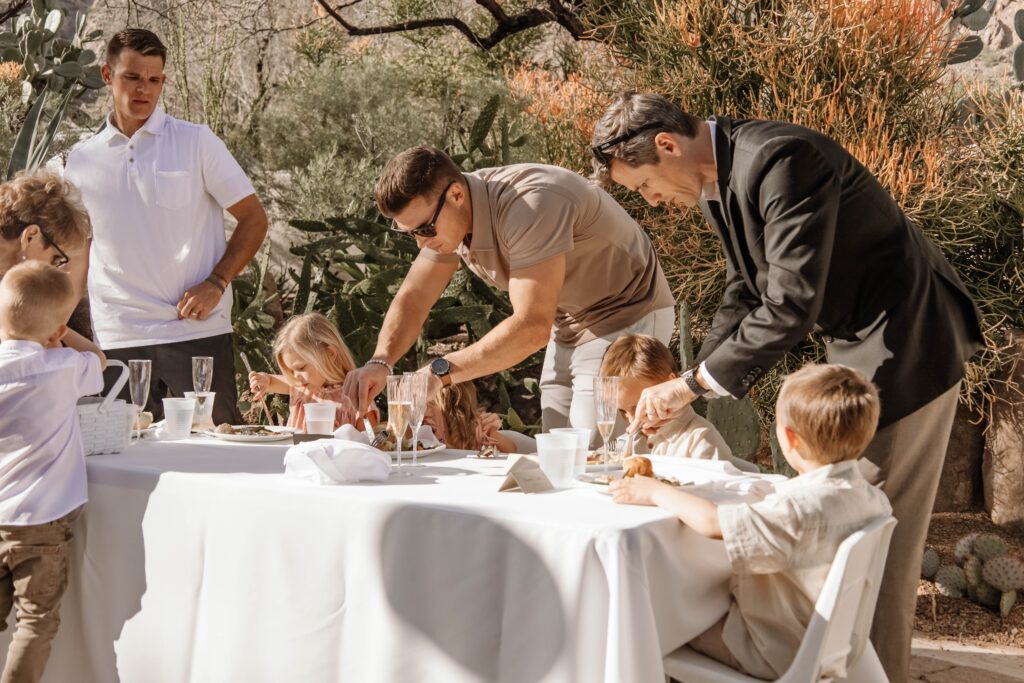 kids table at a backyard wedding while the dads help the with their meal.