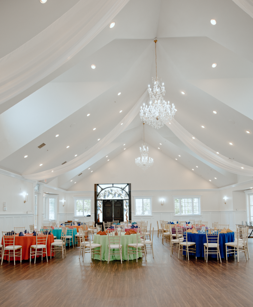 the venue reception with decorated tables and chairs with a white chandelier hanging down