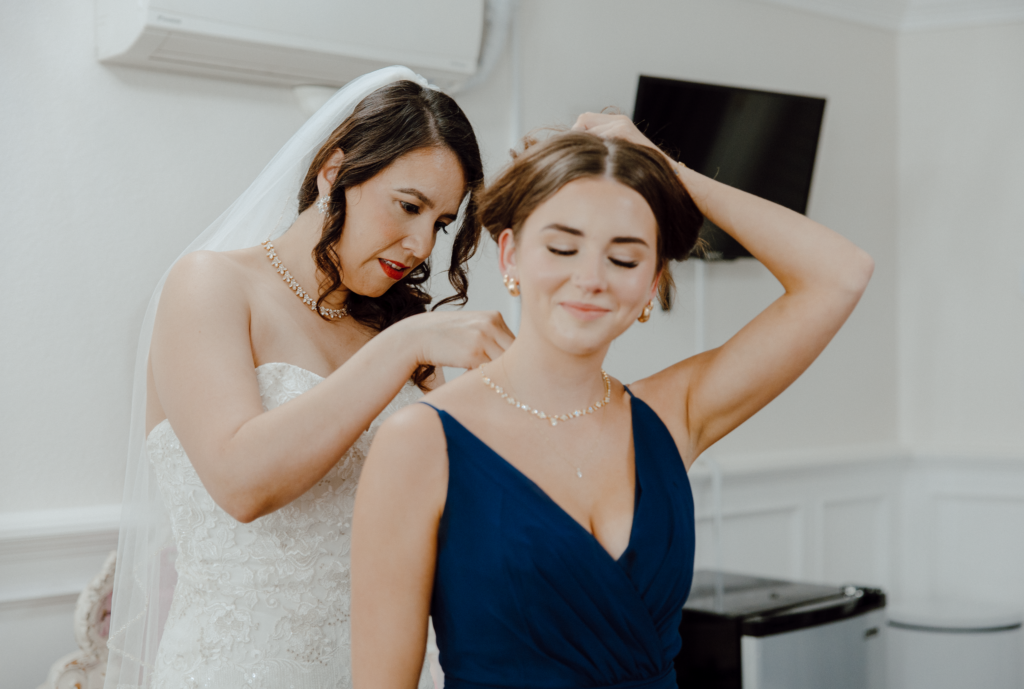 bride putting on a necklace on a bridesmaid.