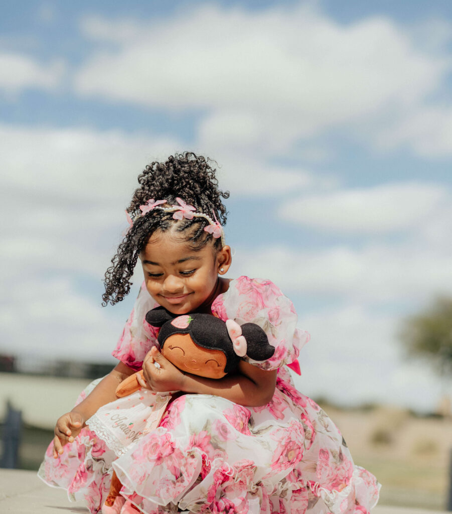 a little black girl holding her black doll and smiling.