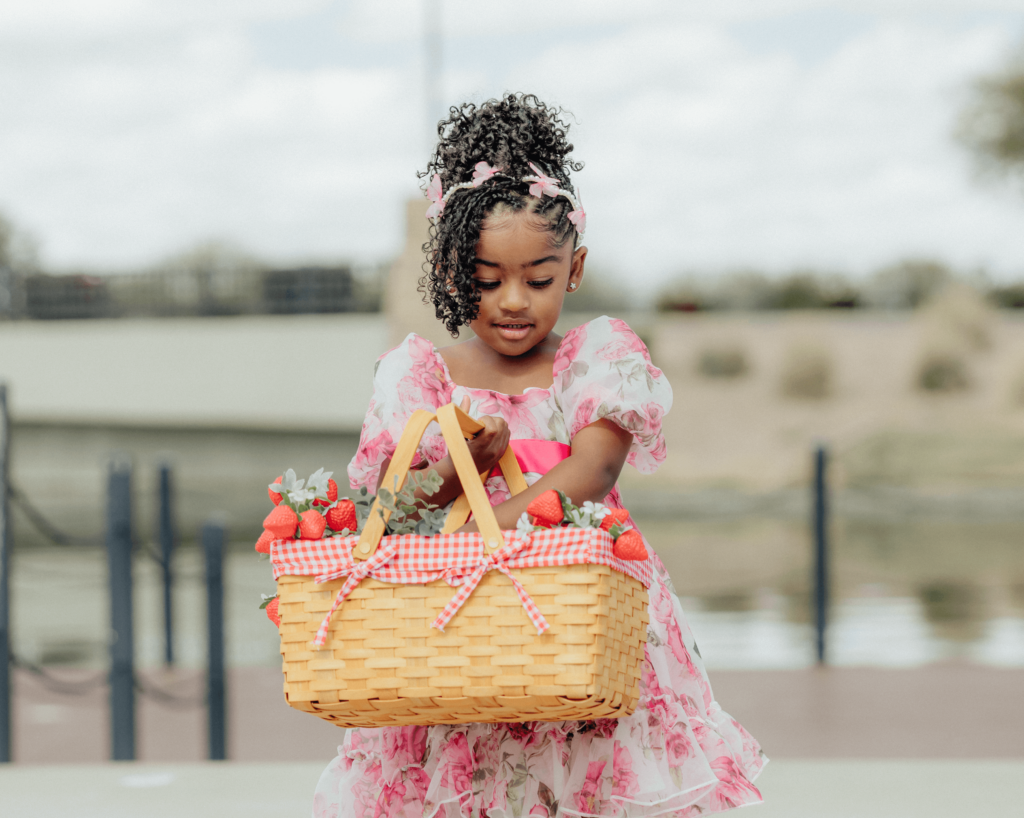 A little girl holding and hugging her basket that has strawberries and she's looking through the basket, 